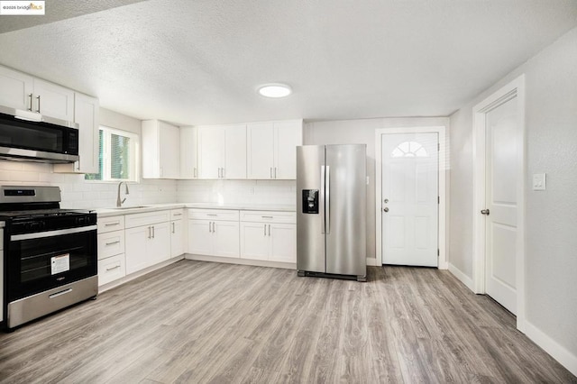 kitchen with sink, backsplash, white cabinetry, and appliances with stainless steel finishes