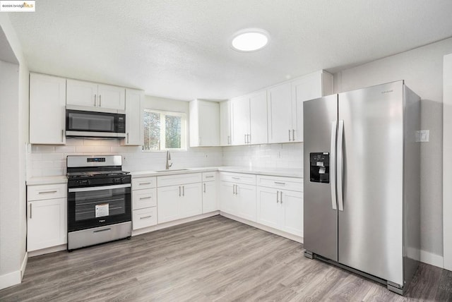 kitchen with white cabinets, stainless steel appliances, sink, backsplash, and light wood-type flooring