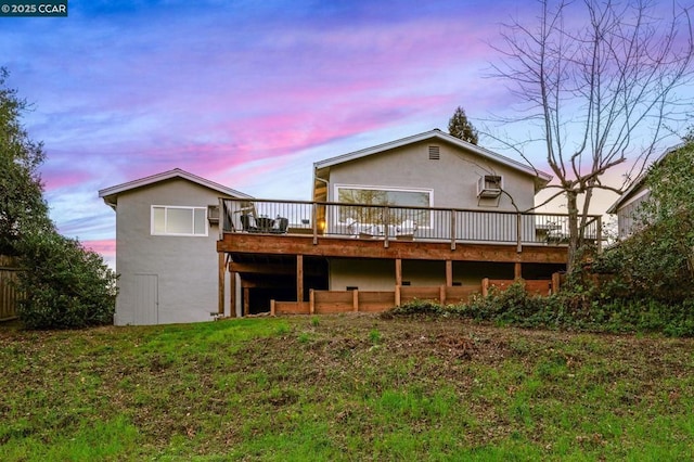 back house at dusk featuring a deck and a lawn