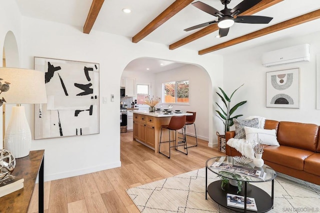 living room with a wall mounted air conditioner, light hardwood / wood-style flooring, beamed ceiling, and ceiling fan