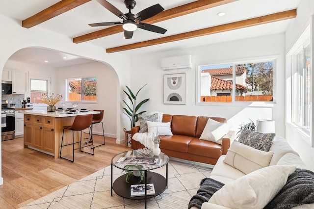 living room with beamed ceiling, an AC wall unit, ceiling fan, and light hardwood / wood-style flooring