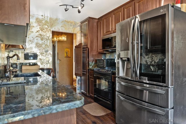 kitchen featuring dark hardwood / wood-style flooring, stainless steel appliances, dark stone counters, sink, and a chandelier