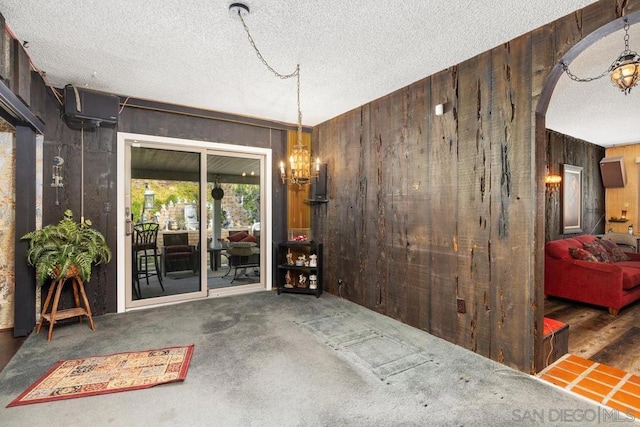 spare room with a textured ceiling, a chandelier, wooden walls, and dark carpet