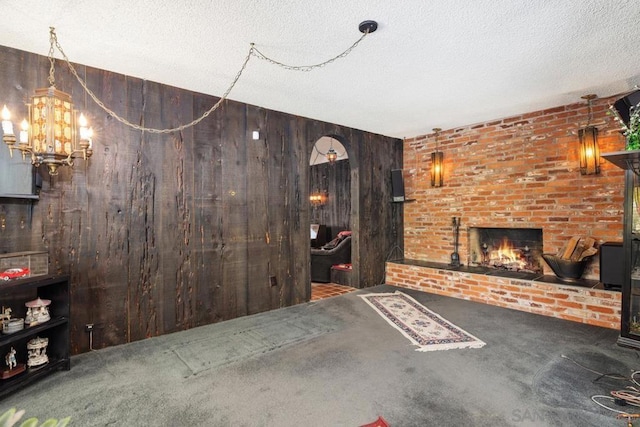 unfurnished living room featuring a fireplace, wood walls, a textured ceiling, and carpet