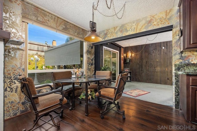 dining area with a textured ceiling, dark hardwood / wood-style flooring, and an inviting chandelier