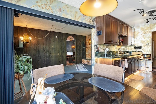 kitchen featuring backsplash, dark brown cabinets, a notable chandelier, and wooden walls