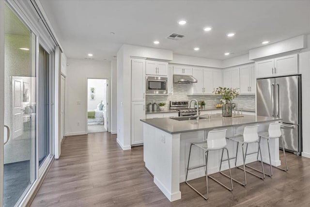 kitchen featuring a kitchen bar, white cabinetry, sink, stainless steel appliances, and a center island with sink