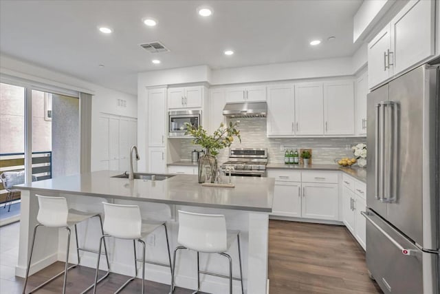 kitchen with white cabinets, stainless steel appliances, tasteful backsplash, sink, and a kitchen island with sink