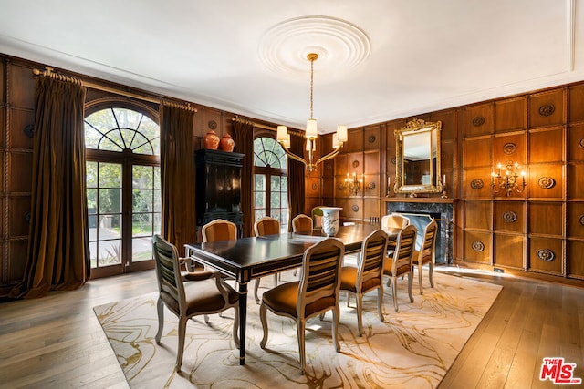 dining space featuring french doors, wooden walls, light hardwood / wood-style floors, an inviting chandelier, and crown molding