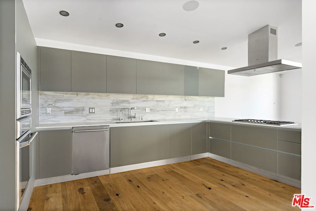 kitchen featuring appliances with stainless steel finishes, sink, light wood-type flooring, gray cabinetry, and island exhaust hood