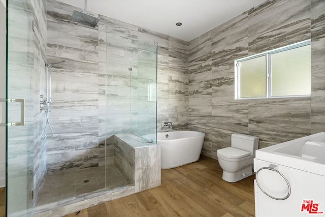 bathroom featuring hardwood / wood-style flooring, tile walls, washer / dryer, and separate shower and tub