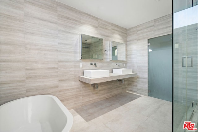 bathroom with dual sinks, tile walls, and separate shower and tub