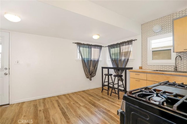 kitchen with light brown cabinetry, sink, gas range oven, tasteful backsplash, and light hardwood / wood-style floors