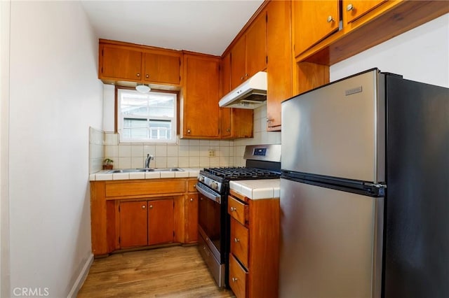 kitchen with sink, backsplash, appliances with stainless steel finishes, and light wood-type flooring