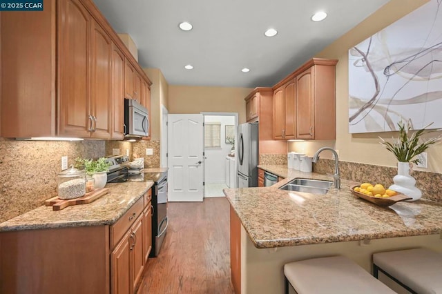 kitchen with sink, kitchen peninsula, light stone countertops, and stainless steel appliances