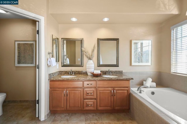 bathroom with toilet, a relaxing tiled tub, and vanity