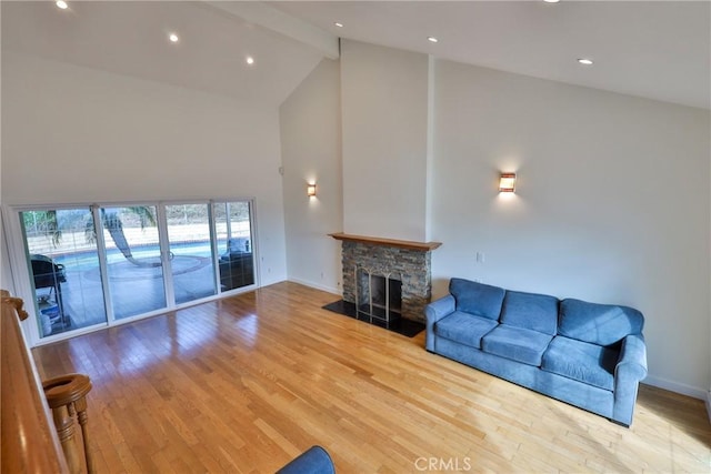 living room featuring beamed ceiling, high vaulted ceiling, light wood-type flooring, and a fireplace