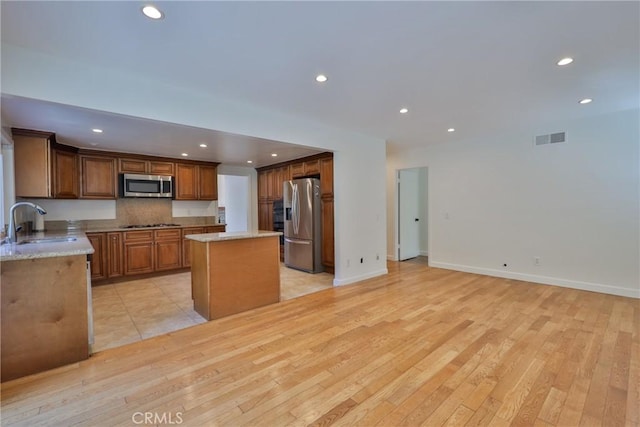 kitchen with sink, light stone counters, light hardwood / wood-style flooring, appliances with stainless steel finishes, and a kitchen island