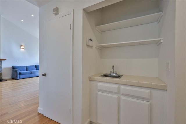 bar with tile counters, sink, light hardwood / wood-style flooring, and white cabinets