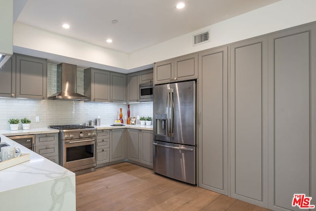 kitchen with wall chimney range hood, stainless steel appliances, light wood-type flooring, and gray cabinets