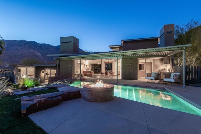 back house at dusk featuring a mountain view, a patio area, an outdoor kitchen, and a fire pit