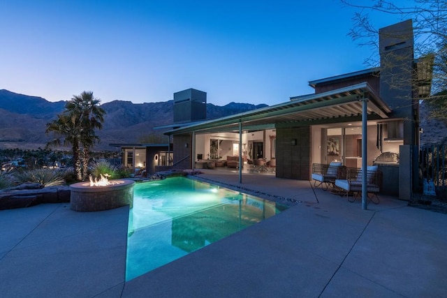 pool at dusk with exterior kitchen, a fire pit, a mountain view, and a patio