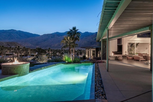 pool at dusk featuring a fire pit, a mountain view, and a patio