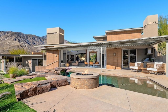 back of property with a mountain view, a patio, and an outdoor fire pit