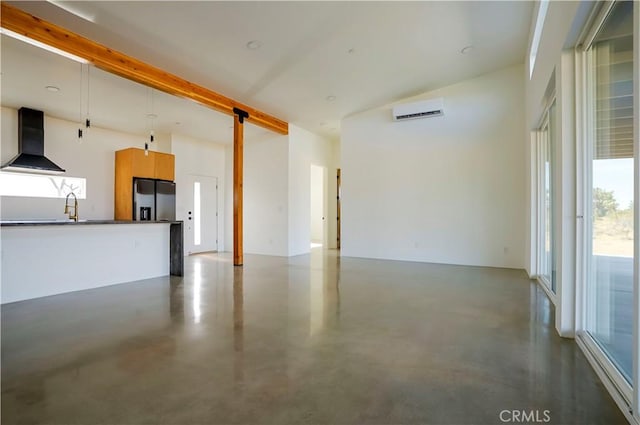 unfurnished living room with sink, a wealth of natural light, a wall mounted AC, and concrete flooring