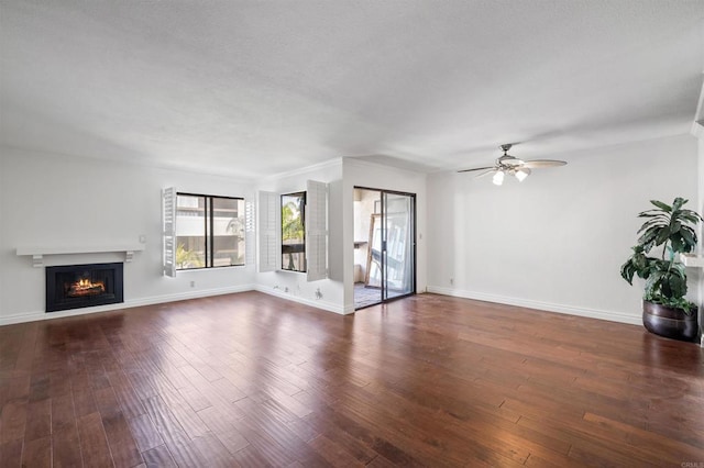 unfurnished living room with baseboards, a warm lit fireplace, wood finished floors, and a ceiling fan