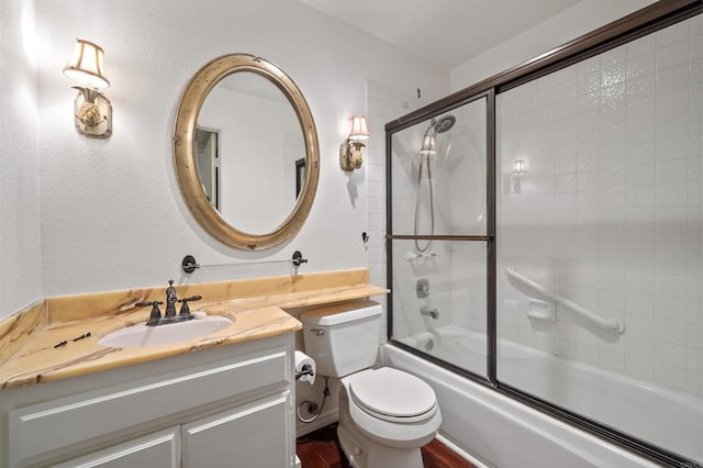 full bath with a textured wall, bath / shower combo with glass door, vanity, and toilet