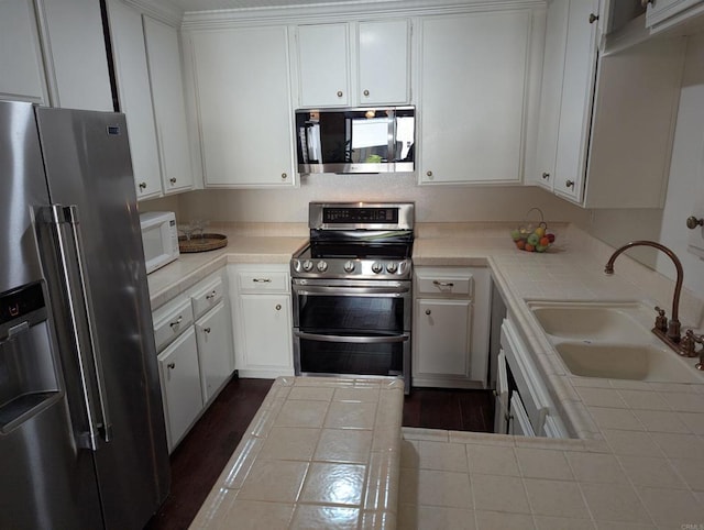 kitchen featuring appliances with stainless steel finishes, tile counters, and white cabinetry