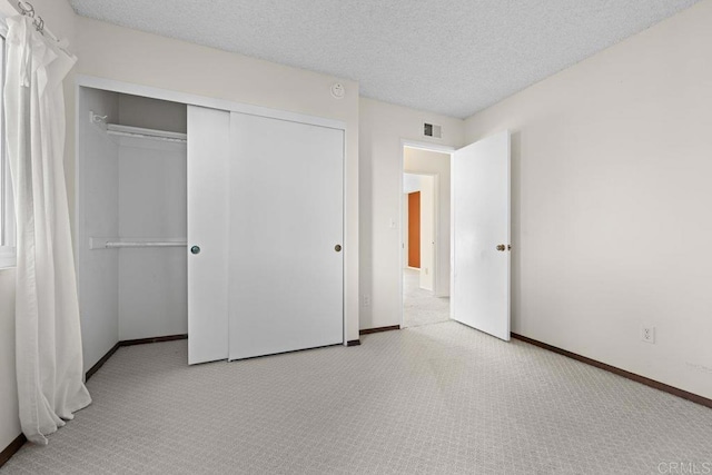 unfurnished bedroom featuring light colored carpet, a textured ceiling, and a closet