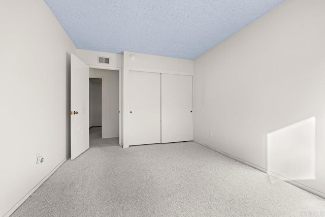 unfurnished bedroom with light carpet, a textured ceiling, and a closet