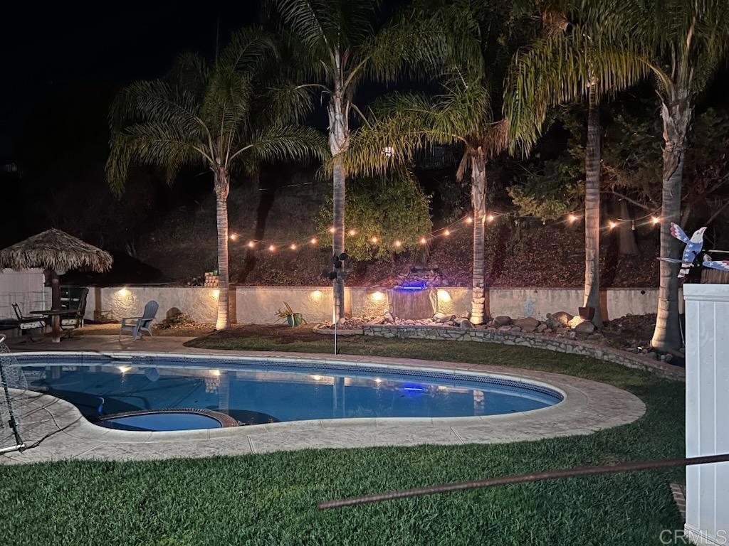 pool at night with an in ground hot tub and a patio