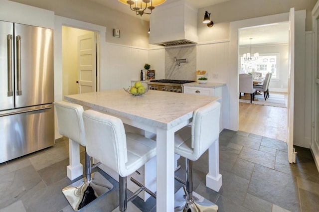 kitchen with high quality fridge, custom exhaust hood, a center island, a kitchen breakfast bar, and white cabinets