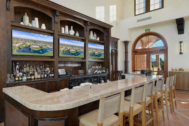 bar with light tile patterned flooring, a high ceiling, and dark brown cabinetry