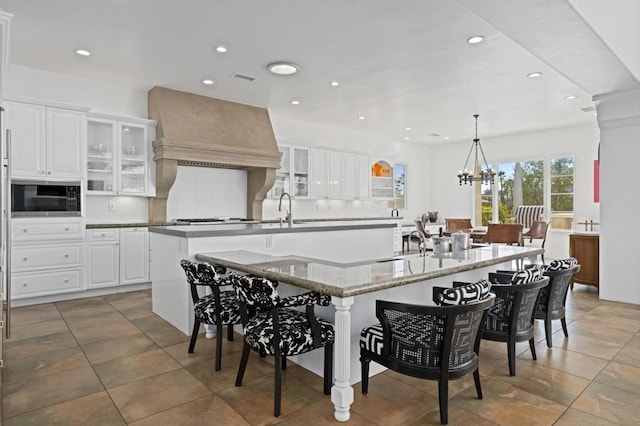 kitchen featuring a spacious island, custom range hood, white cabinets, black microwave, and pendant lighting