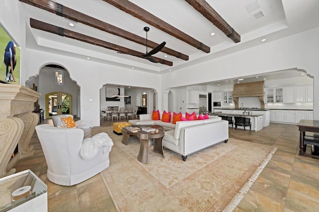 living room with beamed ceiling, a high ceiling, and ceiling fan