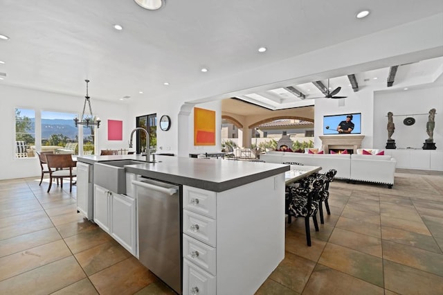 kitchen featuring dishwasher, white cabinetry, beamed ceiling, hanging light fixtures, and a center island with sink