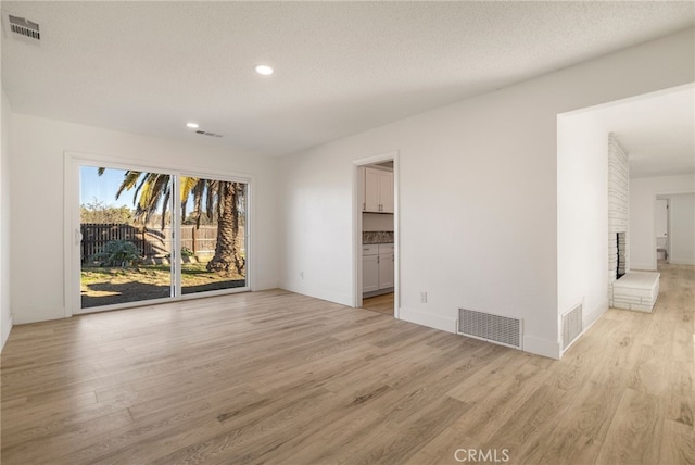 266 E Fig Ln, Corning, CA 96021 - empty room featuring a fireplace, a textured ceiling, and light hardwood / wood-style floors