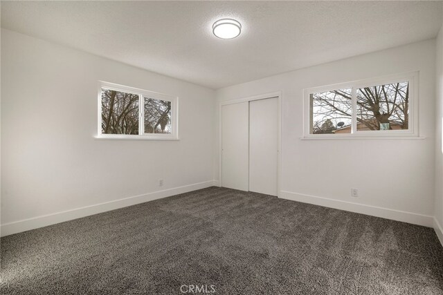 266 E Fig Ln, Corning, CA 96021 - unfurnished bedroom with dark carpet, multiple windows, a closet, and a textured ceiling