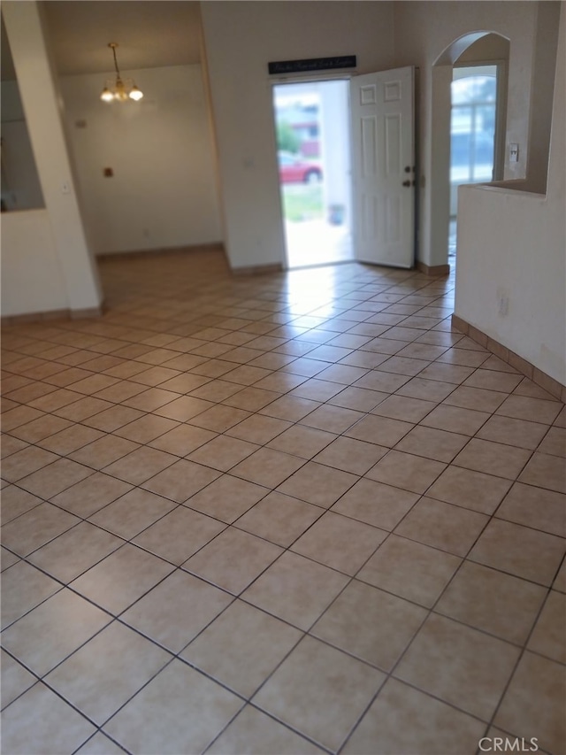 spare room with arched walkways, light tile patterned floors, a chandelier, and baseboards