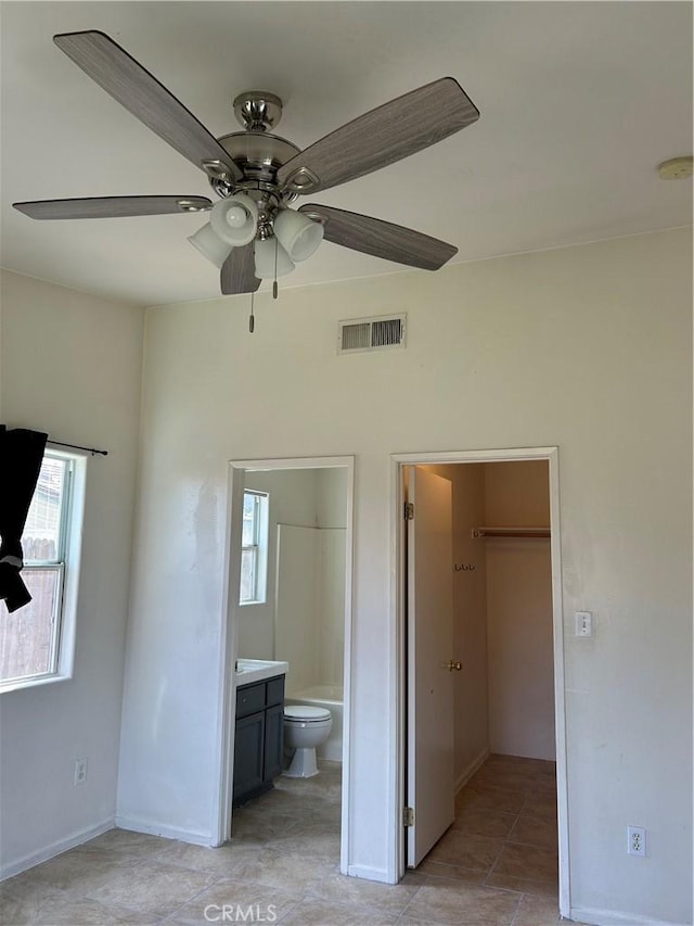 unfurnished bedroom with light tile patterned floors, visible vents, a spacious closet, ensuite bathroom, and a ceiling fan