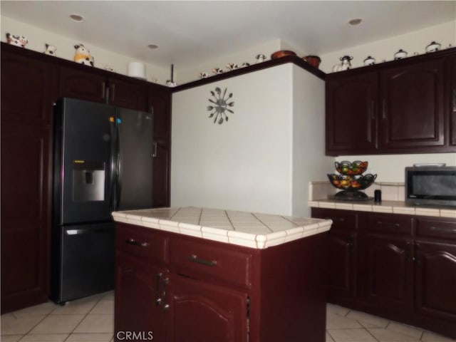 kitchen with light tile patterned floors, tile countertops, black appliances, and a kitchen island