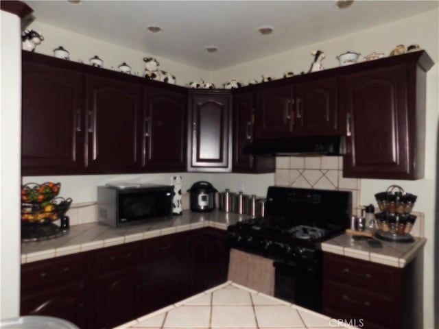 kitchen with range hood, tile counters, light tile patterned floors, dark brown cabinetry, and black appliances