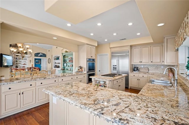 kitchen with light stone countertops, appliances with stainless steel finishes, sink, a kitchen island, and kitchen peninsula