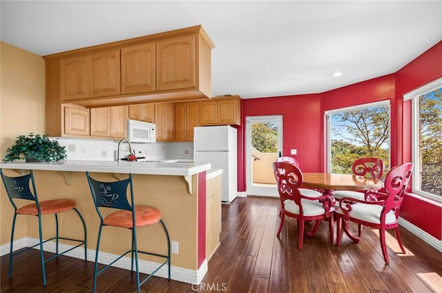 kitchen featuring kitchen peninsula, white appliances, a wealth of natural light, and dark hardwood / wood-style flooring