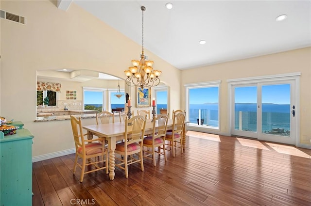 dining area featuring a water view, an inviting chandelier, dark wood-type flooring, and lofted ceiling