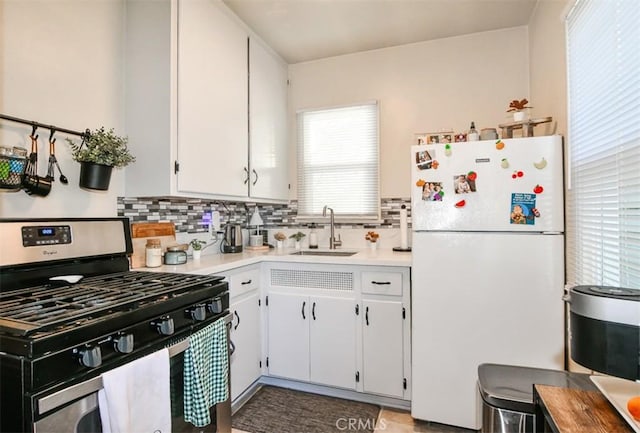 kitchen with stainless steel gas range, white cabinetry, white fridge, sink, and backsplash